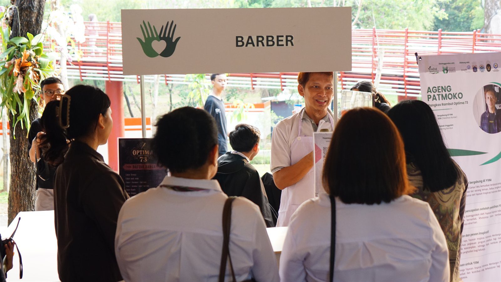 Ageng Patmoko Menyapa Pengunjung Stan Barber Optima 73 Ageng Patmoko mengenakan celemek putih tersenyum menyapa pengunjung di stan barber