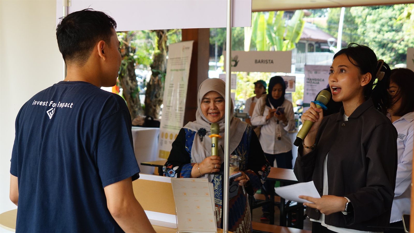Edukasi Literasi Investasi Berdampak Sosial di Stan InvestasIN Pengurus YIIM Diantini Rahayu dan pembawa acara memegang mikrofon di depan stan InvestasIN