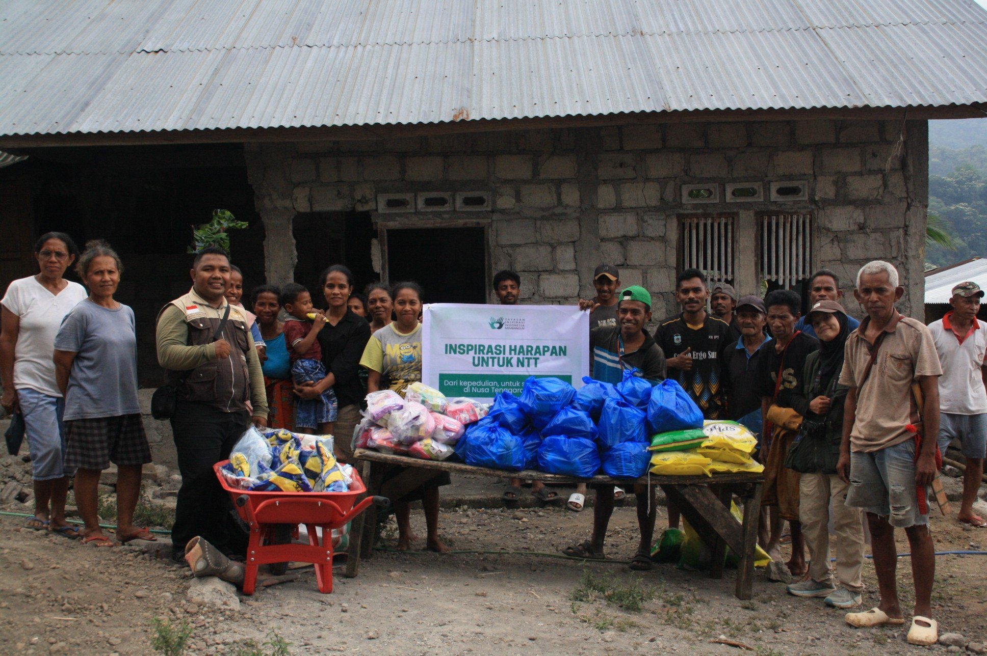 Warga dan relawan berfoto bersama memegang spanduk Inspirasi Harapan untuk NTT di lokasi distribusi bantuan logistik