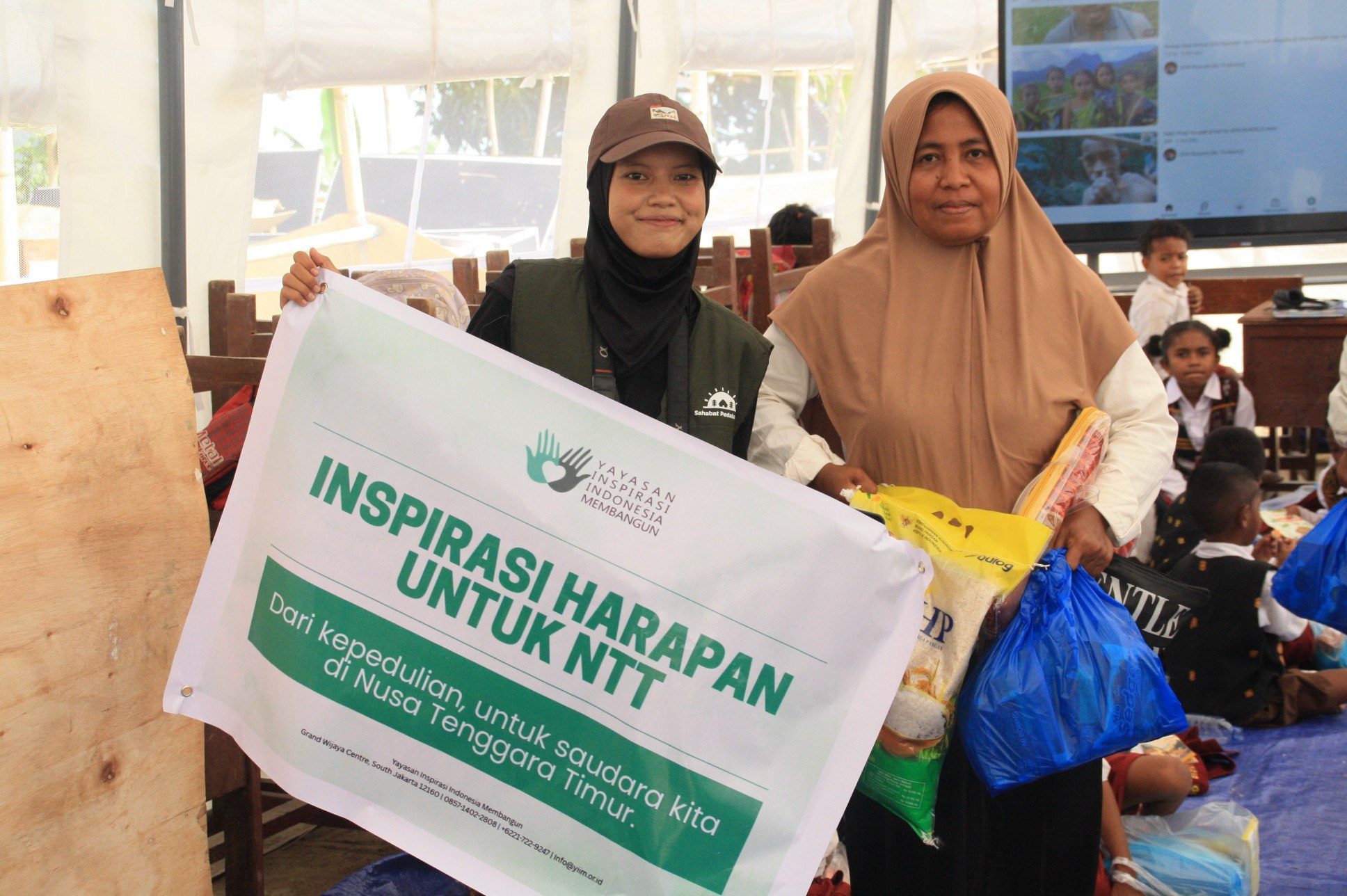 Penyerahan Bantuan Paket Sembako untuk Warga Terdampak Gempa di Flores NTT Relawan membentangkan spanduk kemanusiaan bersama seorang ibu penerima bantuan paket sembako di tenda darurat